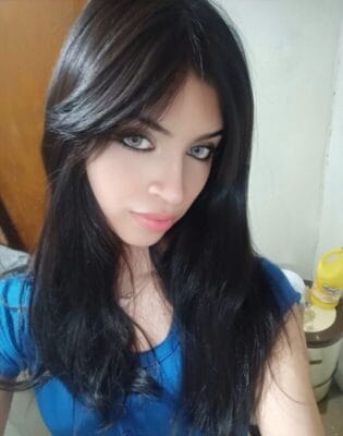 Woman with long dark hair and blue shirt looking at the camera, with pale eyes and soft makeup.
